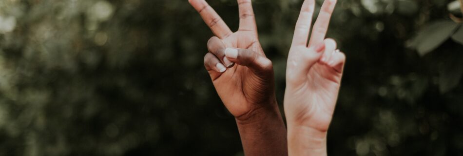 Two hands with difference skin tones holding up peace signs.