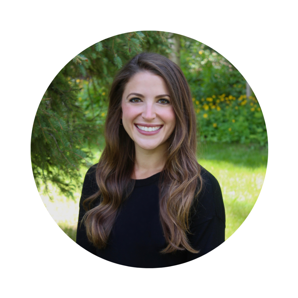 Alexa, a Caucasian female with brown hair and brown eyes smiling in front of greenery.