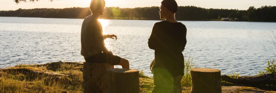 Two people chatting by a lake at golden hour.