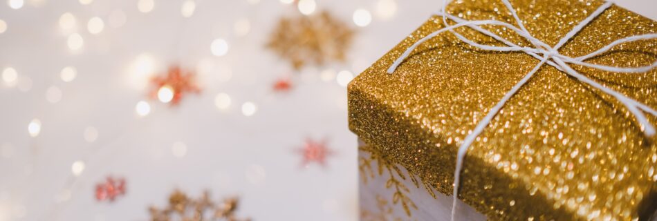 A gold and white holiday gift box with glitter and snowflakes.