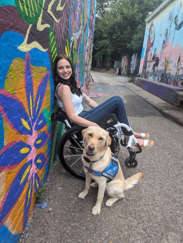 A picture of Aspen Sage using her wheelchair with her yellow Lab, Jojo.