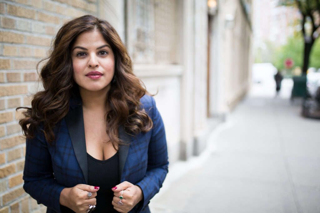 A southeast Asian woman with luscious brunette hair wearing a navy blazer soft smiling. 