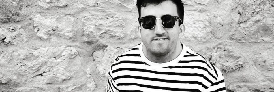 Myles Pearson, a disabled man wearing sunglasses softly smiling.
