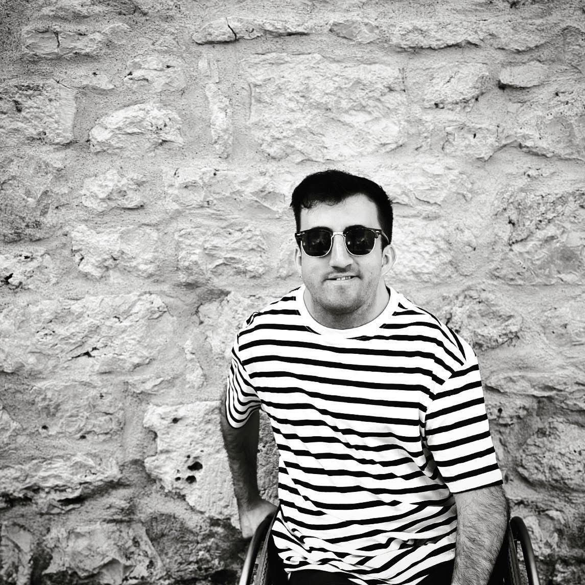 Myles Pearson, a disabled man wearing sunglasses softly smiling.